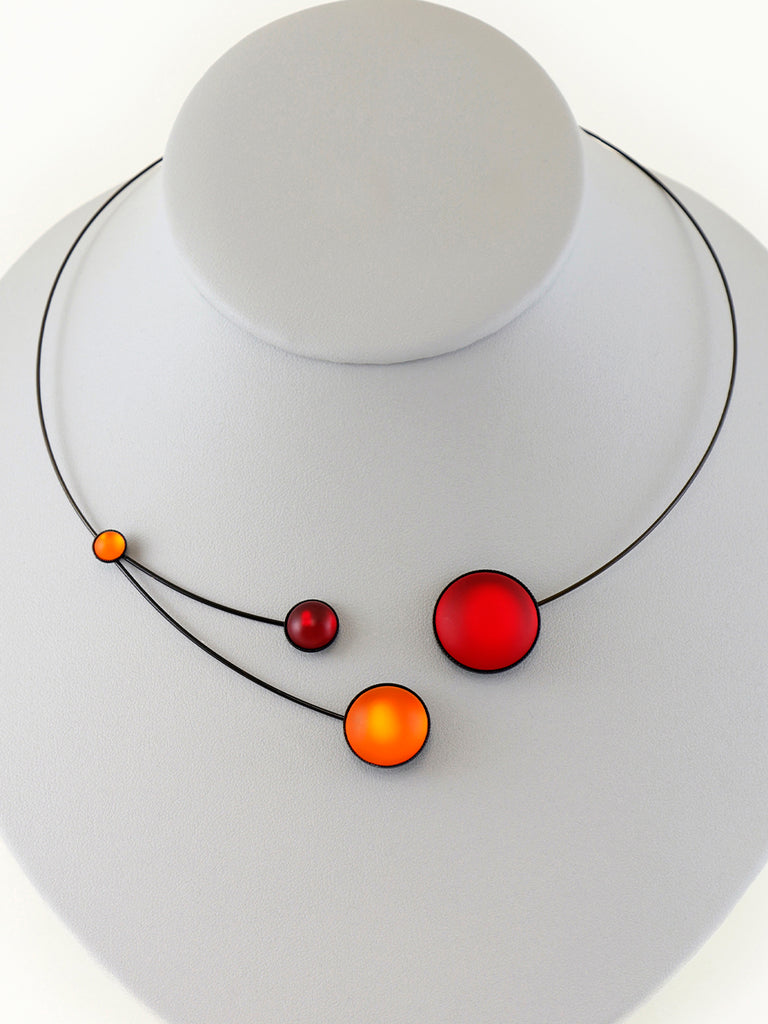 Necklace with red and orange glass beads on a gray display