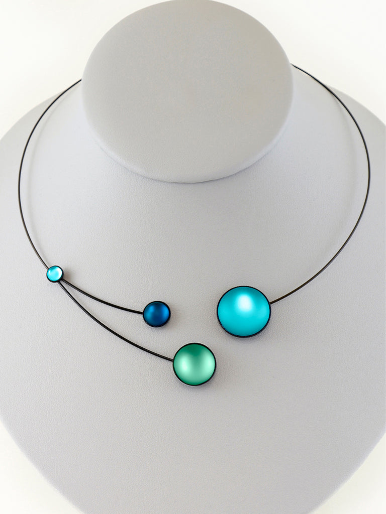 Necklace with blue and green glass beads on a gray display